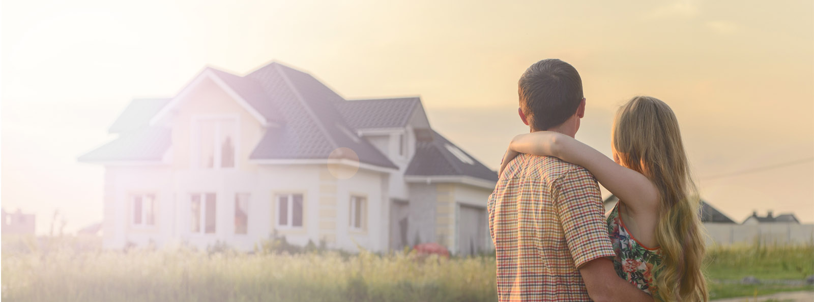 young couple hugging while admiring their new home in the background