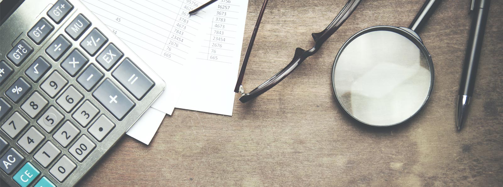 calculator, magnifying glass, glasses, pen, and financial documents lying on table