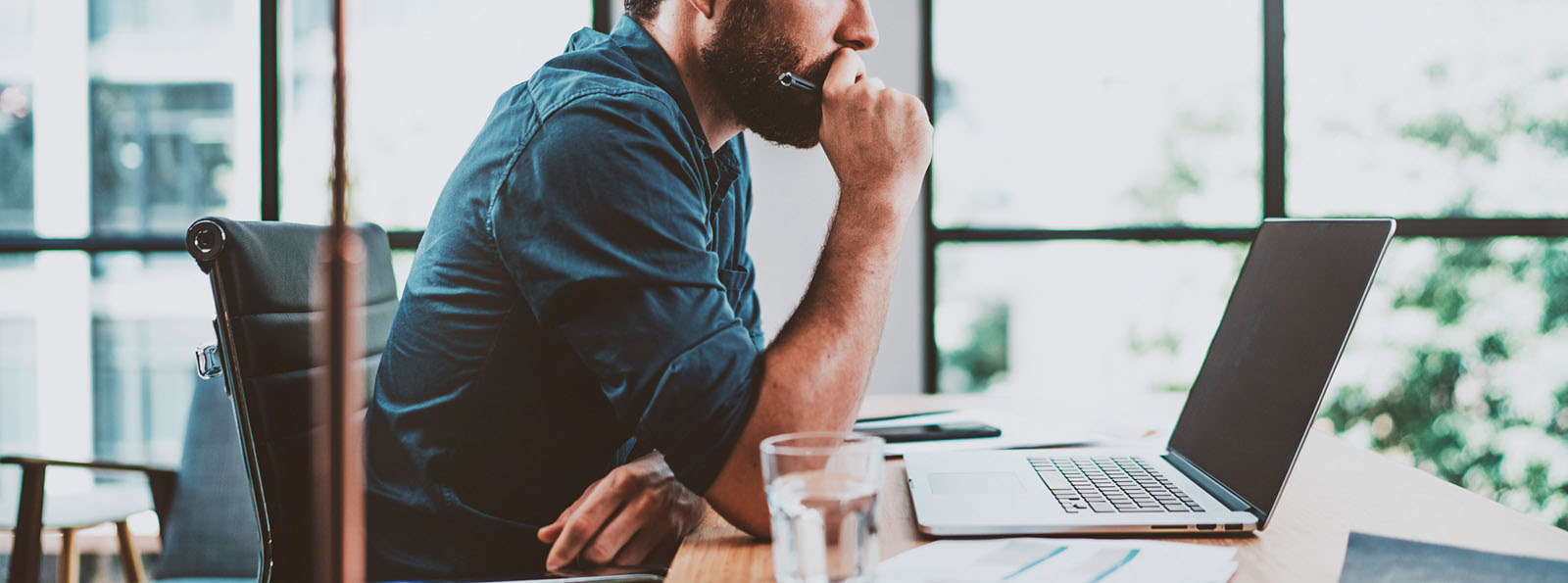 man thoughtfully sitting at desk working on computer